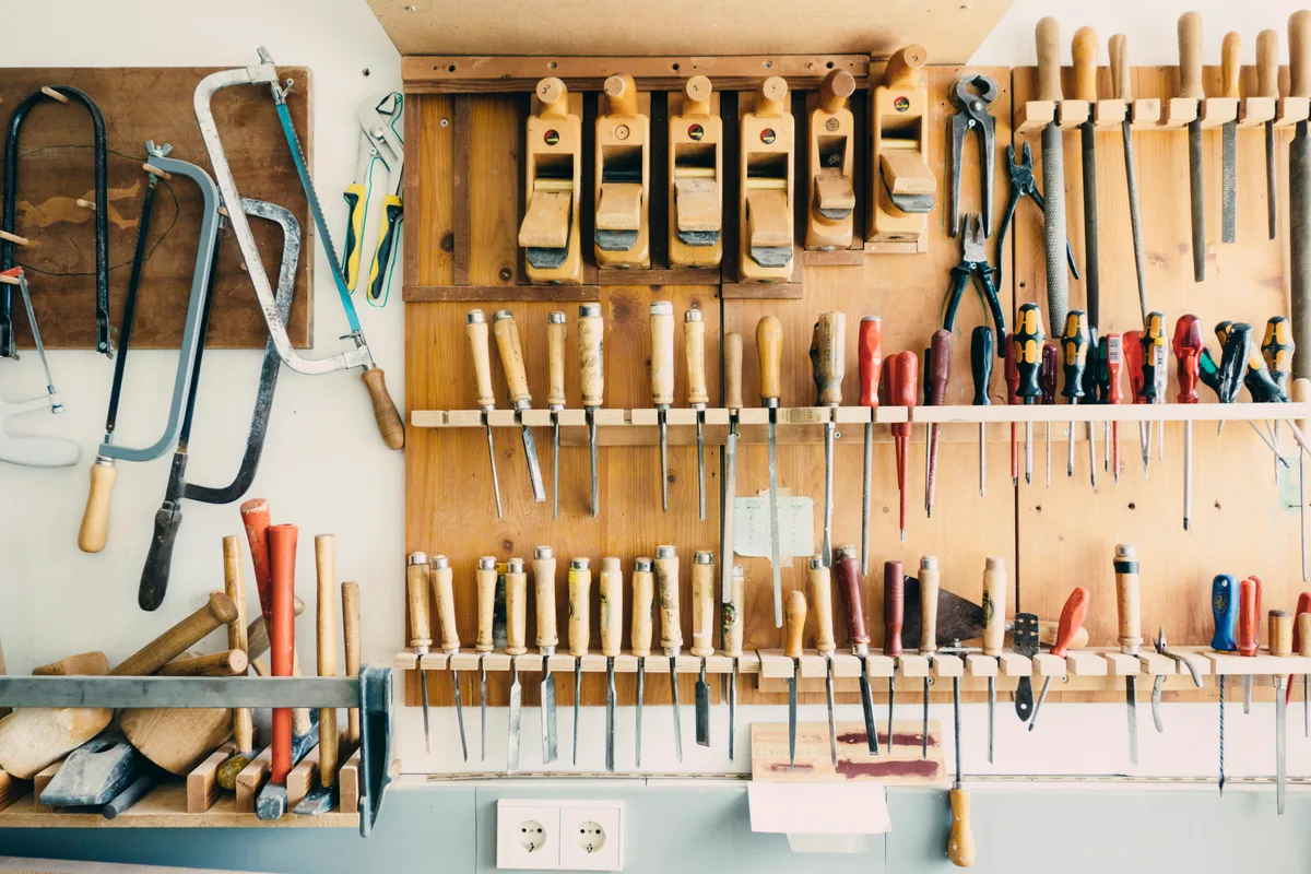 A workshop wall of hand tools, each on its own hook or slot: saws, a row of wooden planes, chisels, screwdrivers and pliers.
