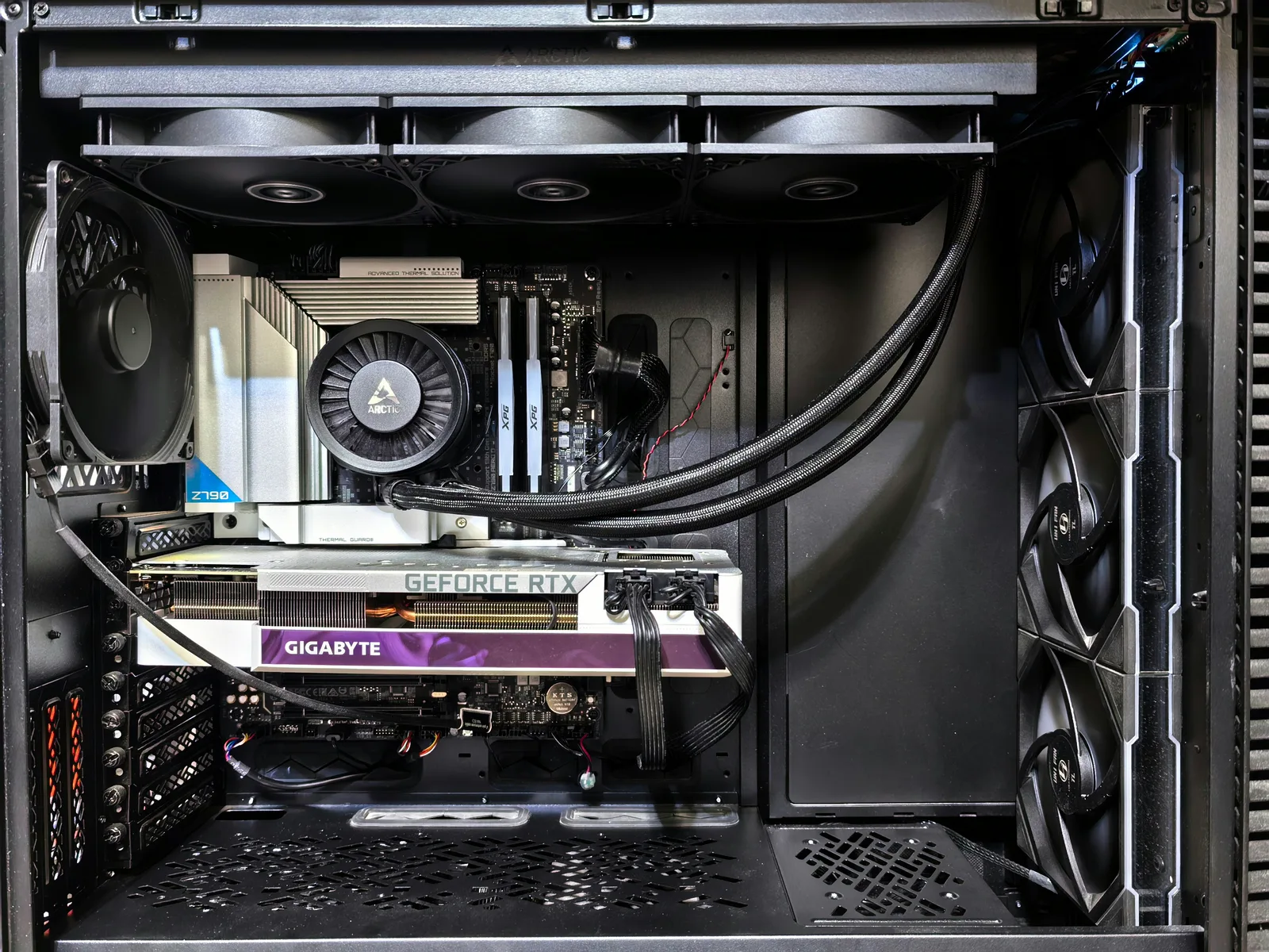 The open side of a desktop workstation: a large graphics card mounted low in the case, a liquid cooler's radiator and three fans across the top, and coolant tubes running between them.