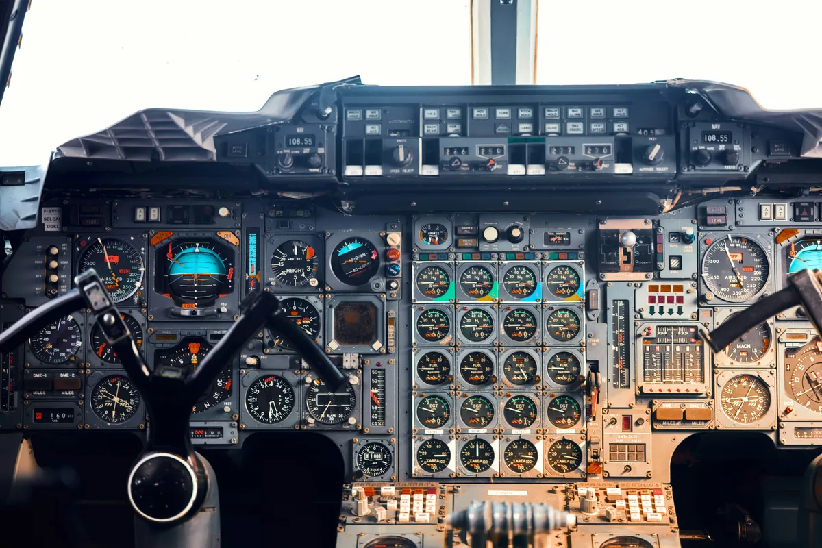 An airliner cockpit seen from behind the seats, its whole front panel covered in rows of round analog dials, each one reporting a single reading.